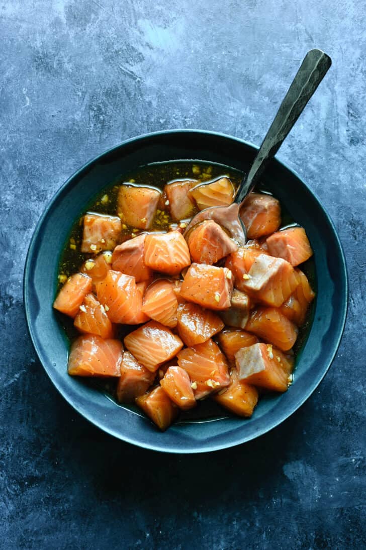 Bite-sized salmon nuggets soaking in a marinade in a blue bowl.