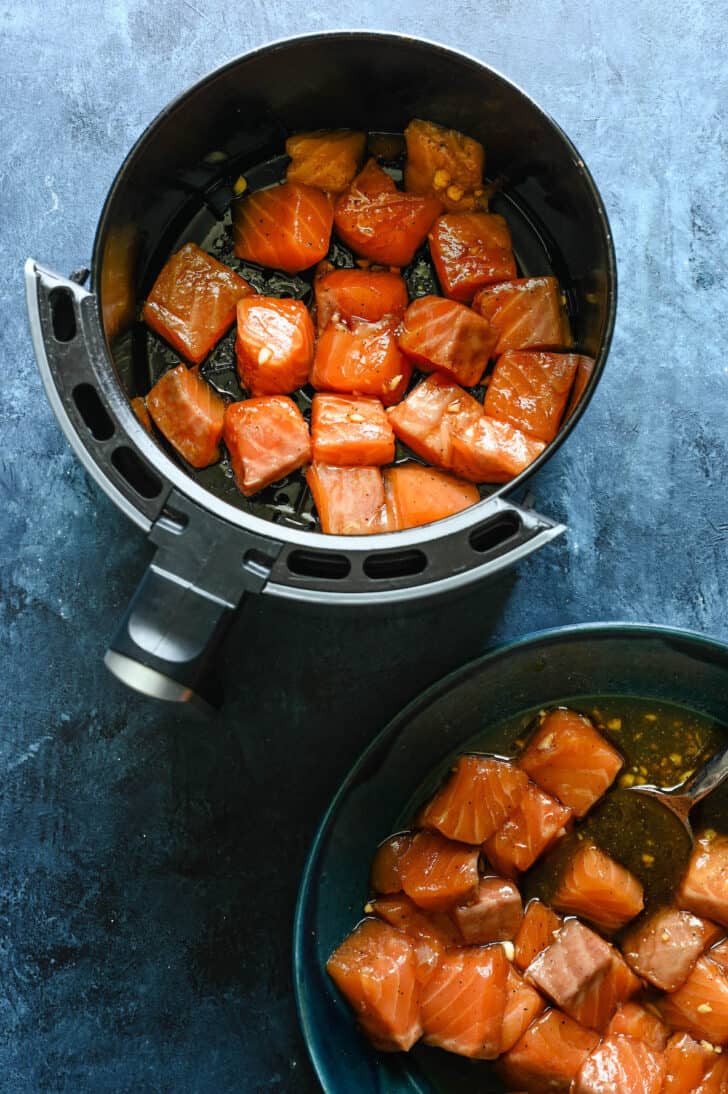 An air fryer basket filled with raw cubes of fish.