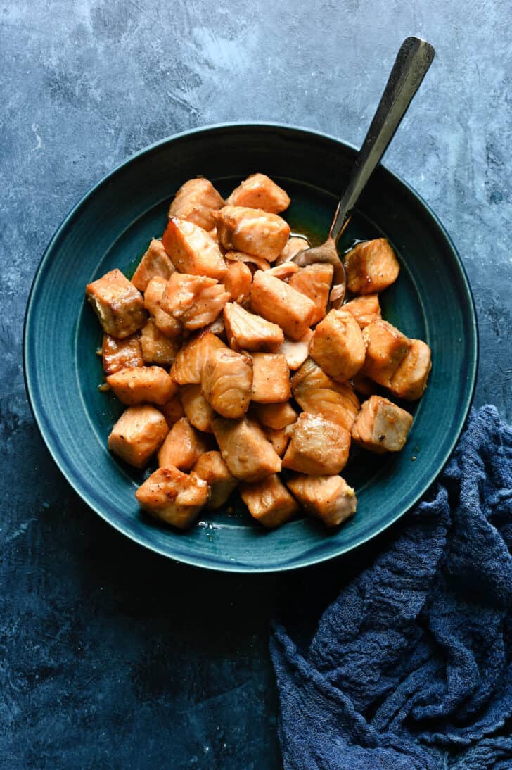 A blue bowl filled with cooked cubes of pink fish.