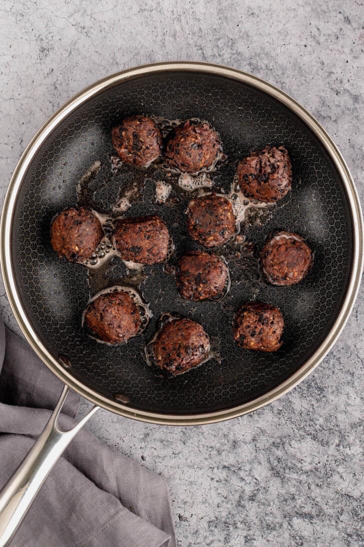 Bean balls being pan fried in a nonstick skillet.