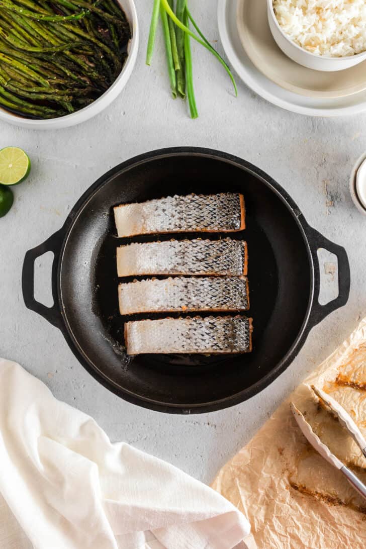 Four pieces of fish, skin side up, in cast iron skillet.