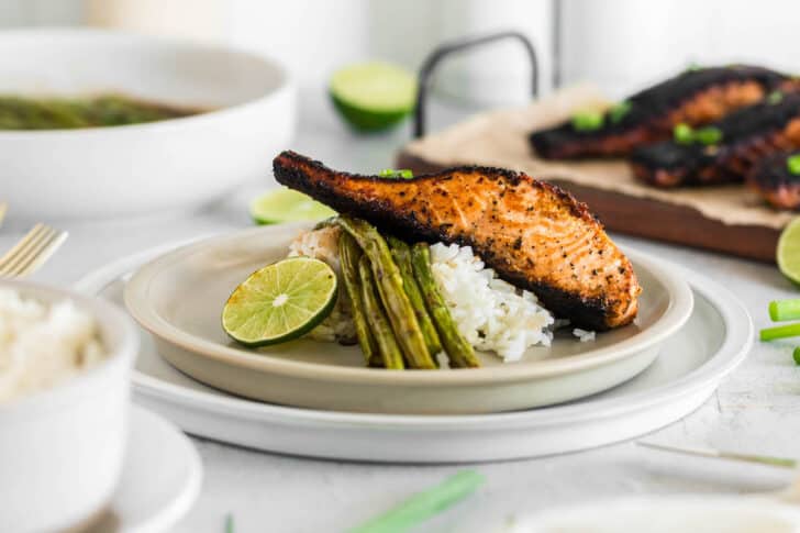 A piece of blackened salmon on top of white rice and asparagus with a lime garnish.