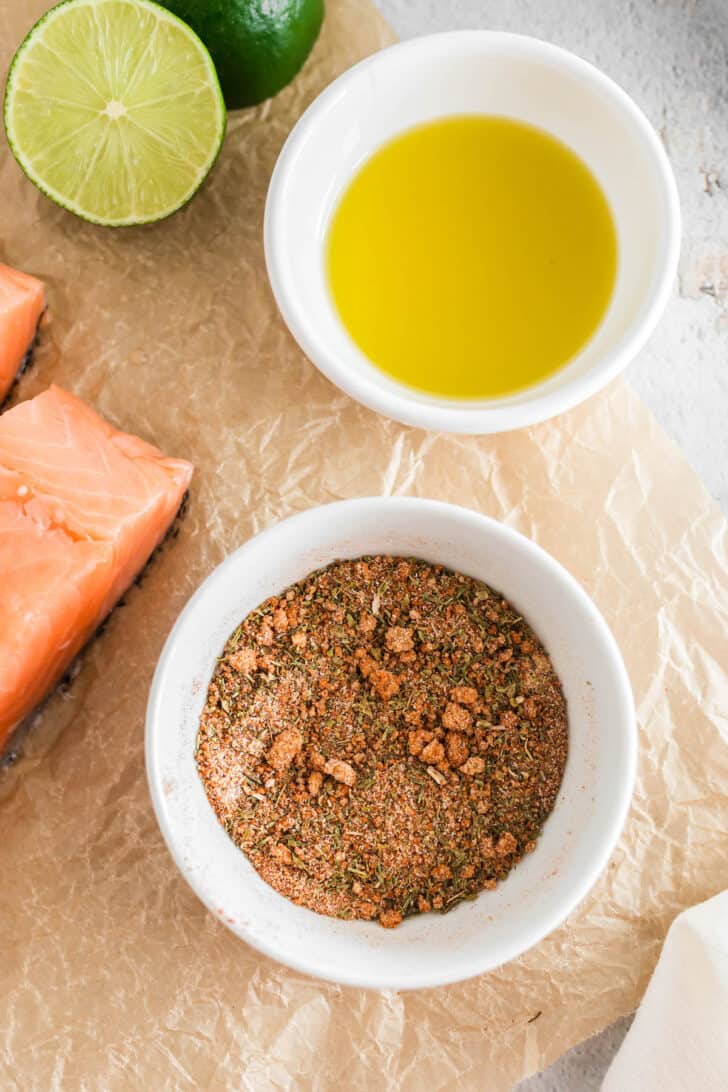 Two small white bowls. One is filled with a spice mixture and the other is filled with olive oil.