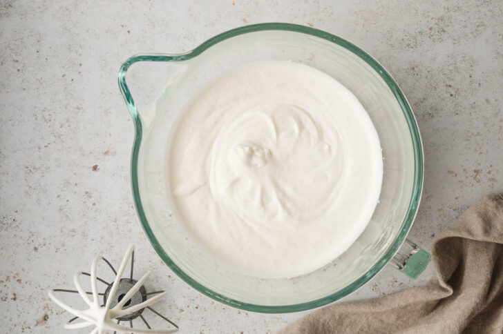 A glass stand mixer bowl filled with heavy cream, whipped to soft peaks.