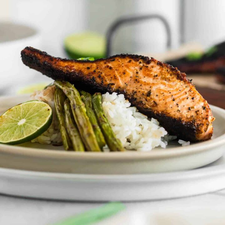 A piece of blackened salmon on top of white rice and asparagus with a lime garnish.