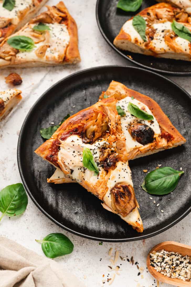 Two slices of grilled chicken pizza garnished with basil on a dark plate.