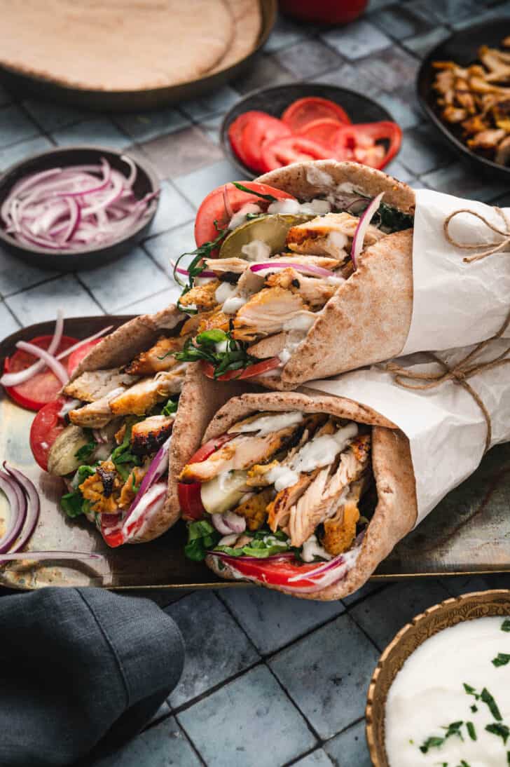 Three chicken shawarma wrap sandwiches wrapped in paper on a metallic tray.