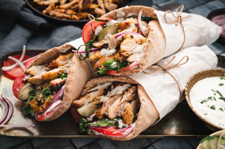 Three chicken shawarma wrap sandwiches wrapped in paper on a metallic tray.