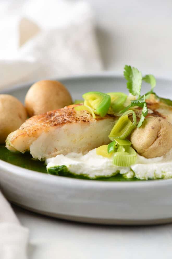 A Chilean sea bass recipe topped with leeks and cilantro, with yogurt, green sauce and potatoes.