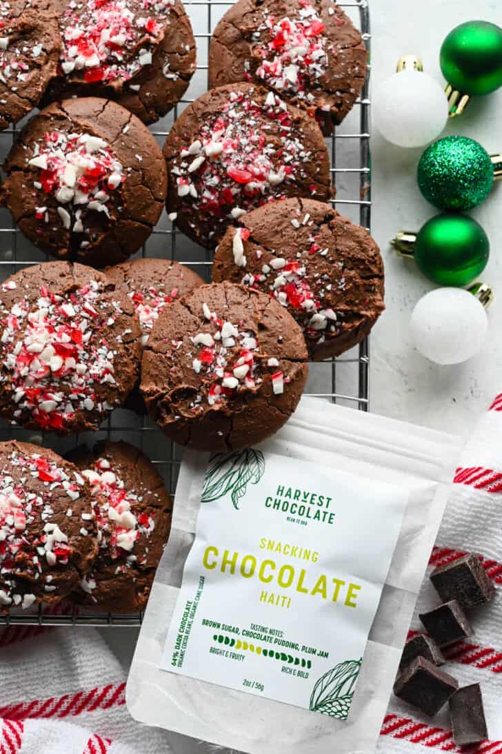 Chocolate Peppermint Cookies on a wire rack with small green and white bulb ornaments decorating the scene, as well as a bag of Harvest Chocolate Haiti Snacking Chocolate.