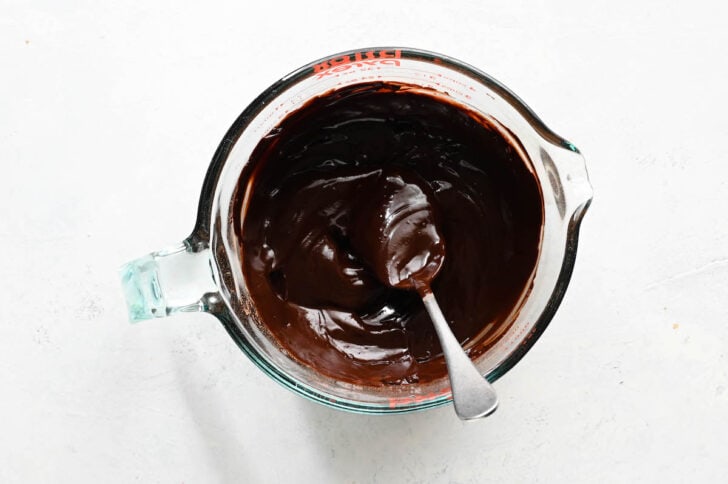 A large glass measuring cup with a spoon stirring a melted chocolate mixture.