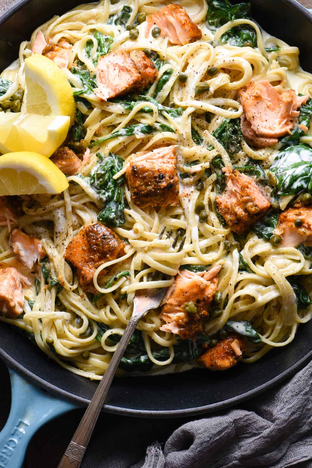 Closeup on a fork twirling a bite of creamy salmon pasta. Spinach and capers dot the pasta dish.