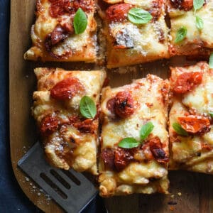 Closeup of Detroit style pizza topped with tomatoes and basil.