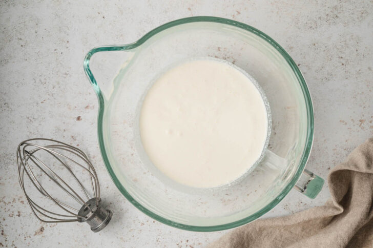 A glass stand mixer bowl filled with heavy cream.