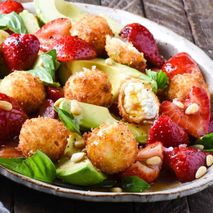 A large platter filled with fried goat cheese balls, strawberries, avocado, pine nuts and basil.