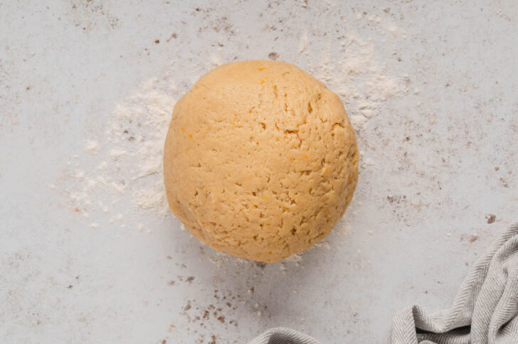 A light brown cookie dough rolled into a large ball on a light work surface.
