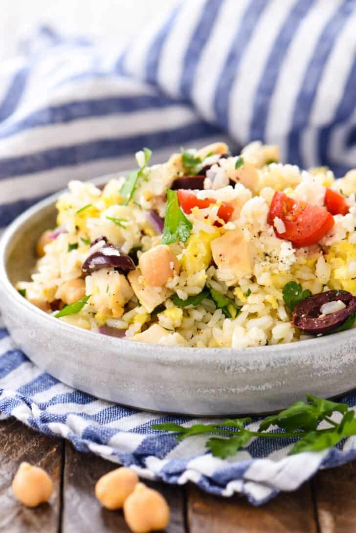 A shallow gray bowl filled with a Greek rice recipe containing chicken, vegetables, chickpeas and feta cheese.