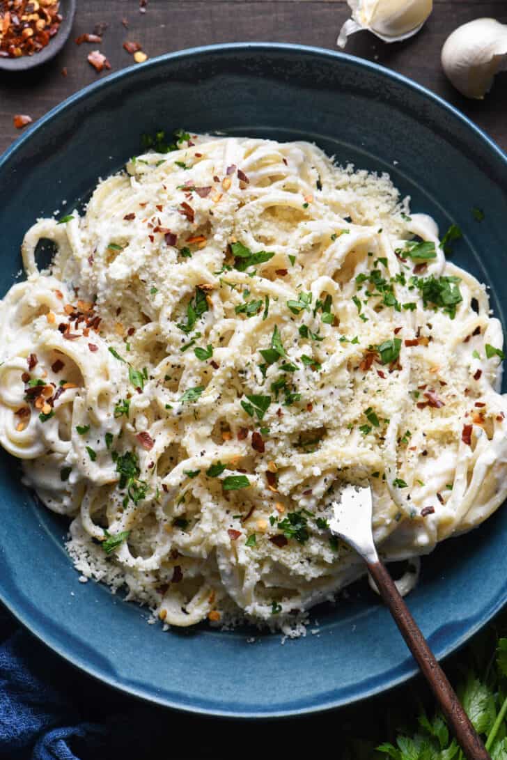 A blue bowl filled with spaghetti tossed with Greek yogurt Alfredo sauce, topped with Parmesan cheese, parsley and red pepper flakes.
