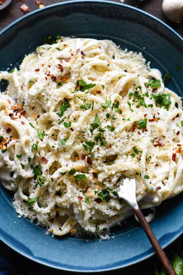 A blue bowl filled with spaghetti tossed with Greek yogurt Alfredo sauce, topped with Parmesan cheese, parsley and red pepper flakes.