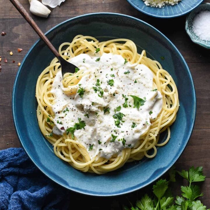 A blue bowl filled with spaghetti topped with Greek yogurt pasta sauce, chopped parsley and red pepper flakes.