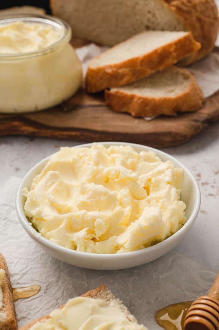A small white bowl filled with homemade butter, with bread in the background.