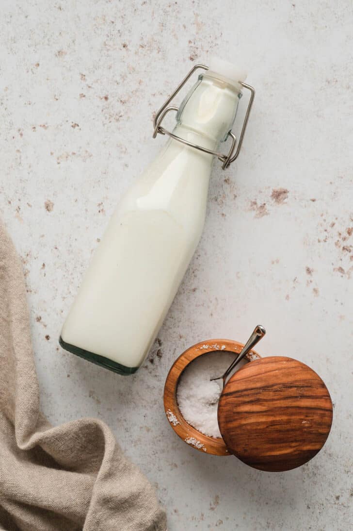 A bottle of cream and a wooden salt keep on a light surface.