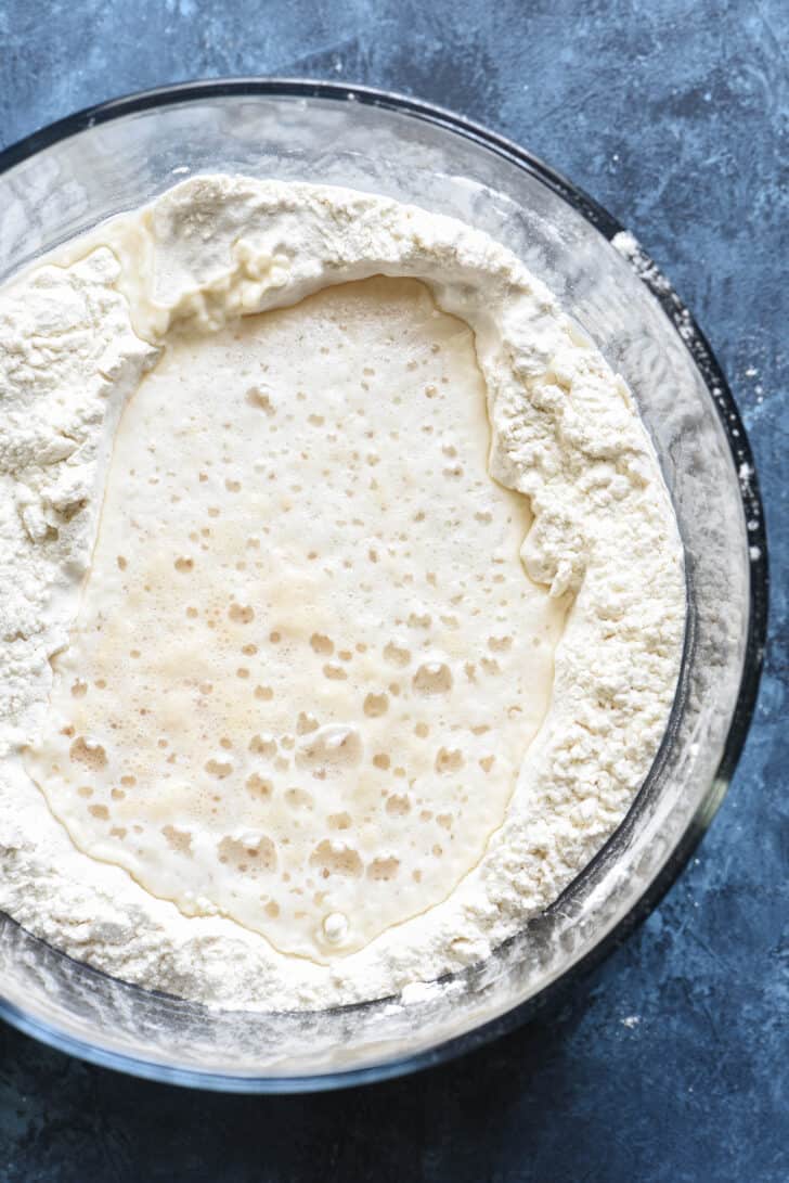 A glass bowl of flour with a well filled with liquid in the middle.