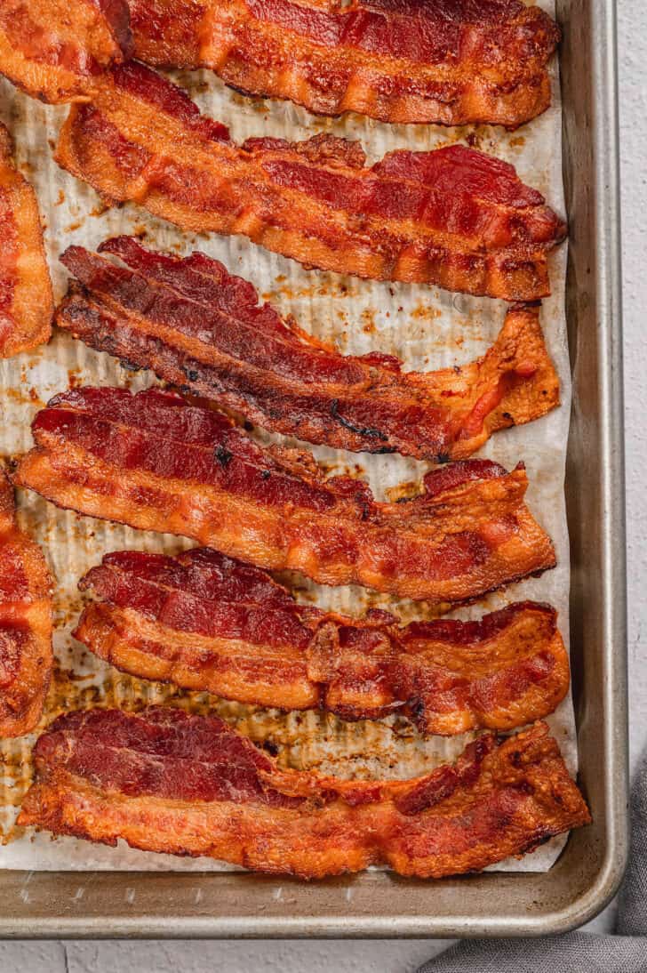 Crispy bacon lined up on a parchment paper lined baking pan.