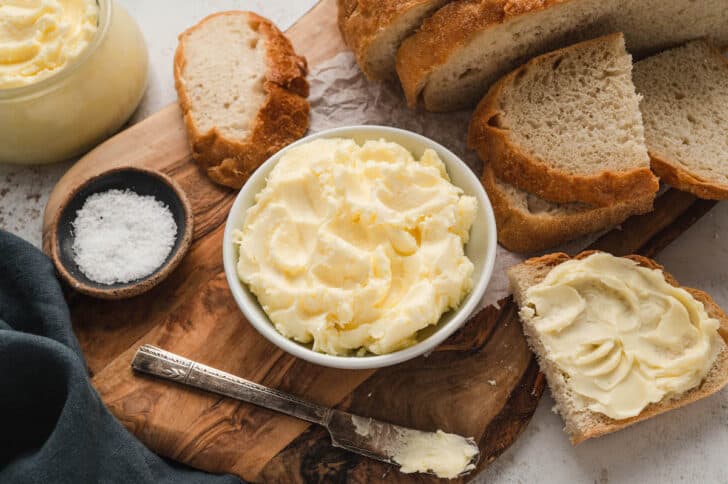 A bowl of homemade butter with sliced bread on a rustic wooden cutting board.