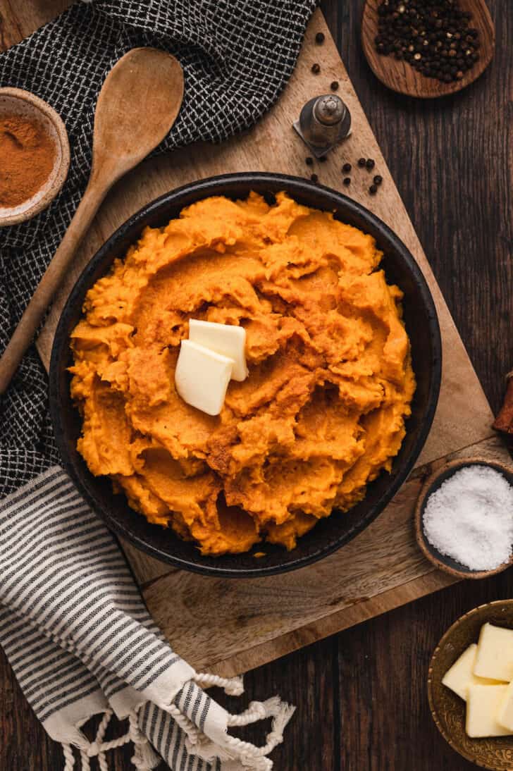 Mashed instant pot sweet potatoes topped with pats of butter in a black bowl.