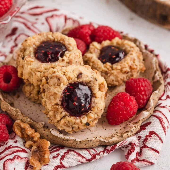 Raspberry thumbprint cookies on a small rustic plate with fresh raspberries.