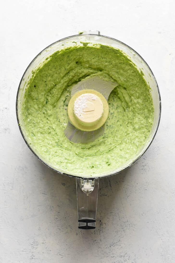 A food processor bowl filled with a creamy green sauce.