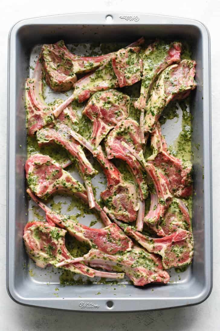 Lamb chops coated in an herby lamb lollipop marinade, in a rectangle metal pan.