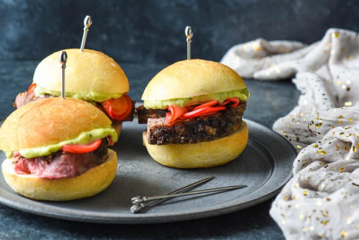 Lamb sliders on small rolls garnished with pickled radishes and pesto mayo, and skewered with decorative silver toothpicks.