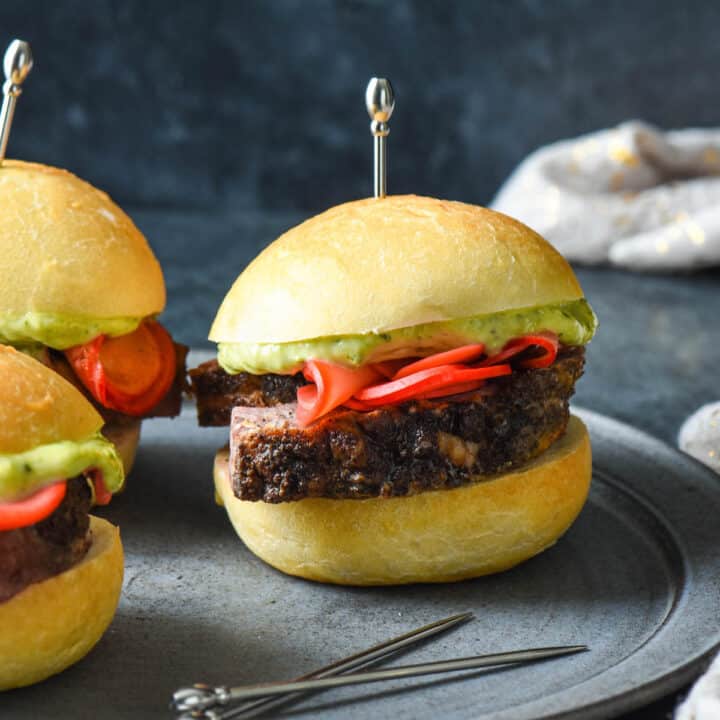 Lamb sliders on small rolls garnished with pickled radishes and pesto mayo, and skewered with decorative silver toothpicks.