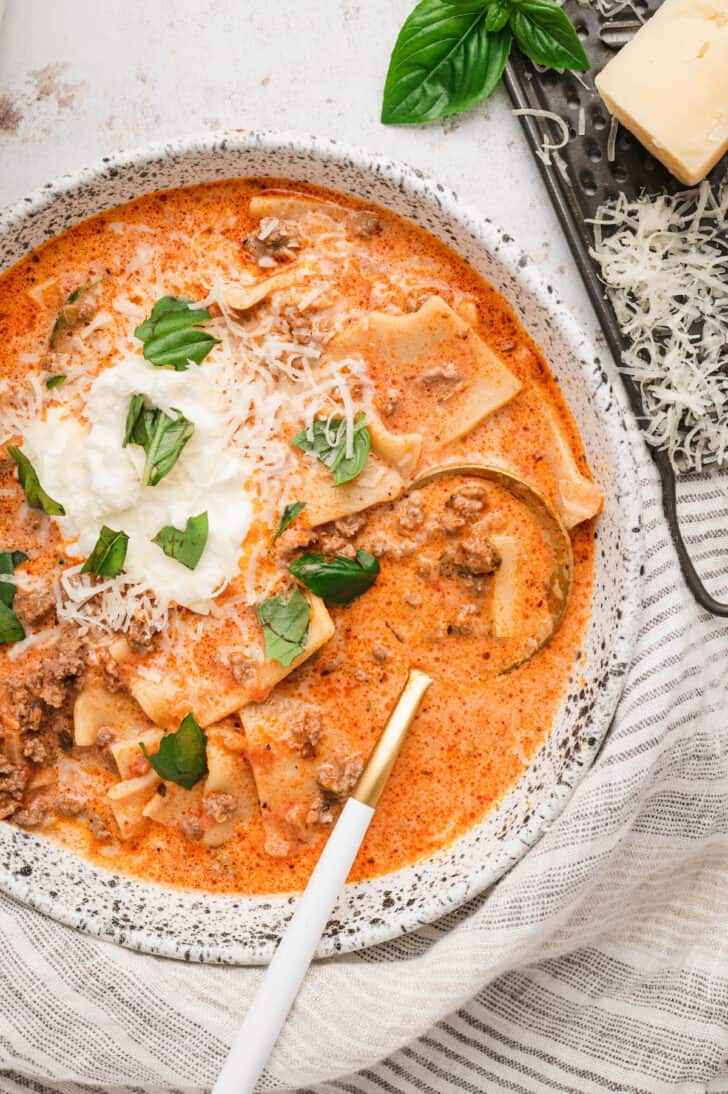 An Easy Lasagna Soup Recipe in a rustic bowl, topped with ricotta, Parmesan cheese and fresh basil.