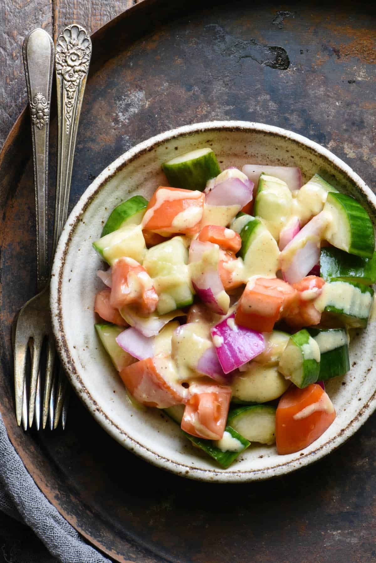 Overhead shot of bowl with chopped salad. Cucumbers, tomatoes and red onions dressed with tahini salad dressing.