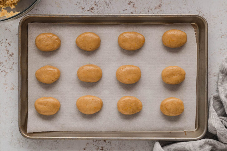 A rimmed baking pan lined with parchment paper, topped with oval-shaped cookies.