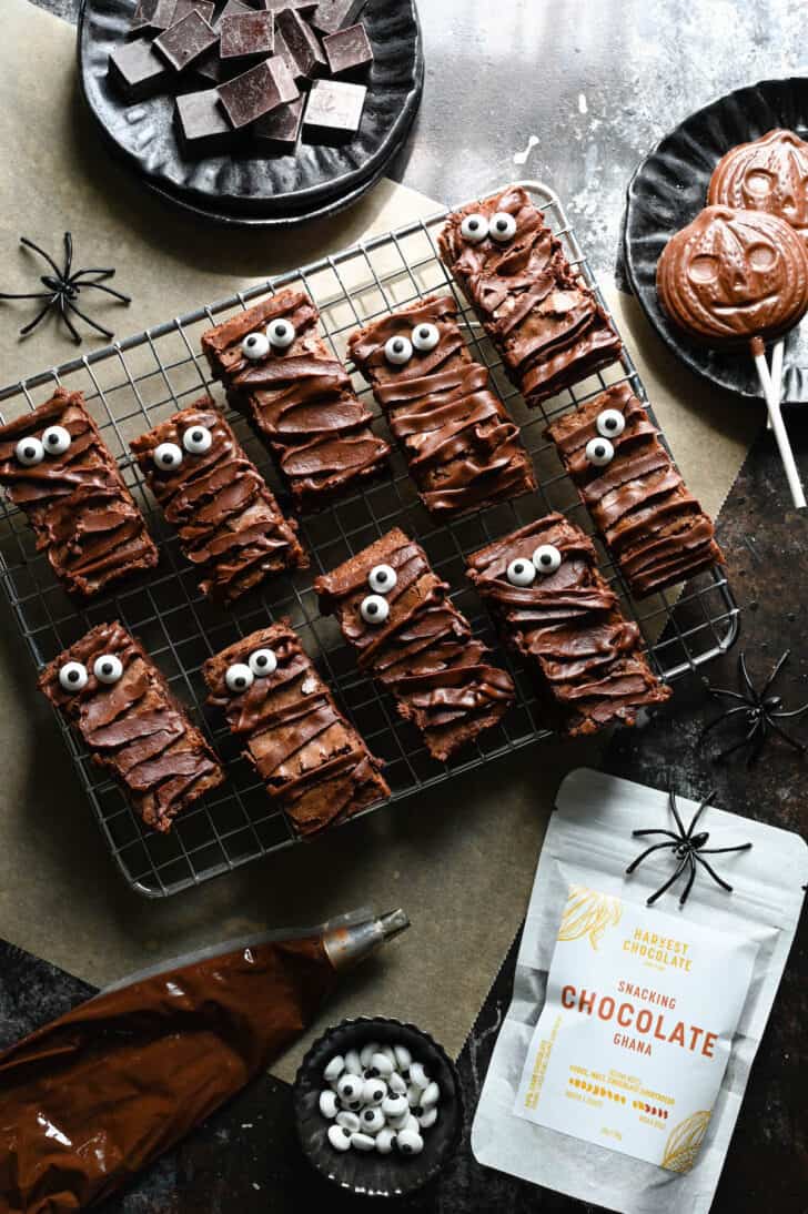 Chocolate ganache brownies with candy eyeballs on a cooling rack with plastic spiders and a bag of Harvest Chocolate nearby.