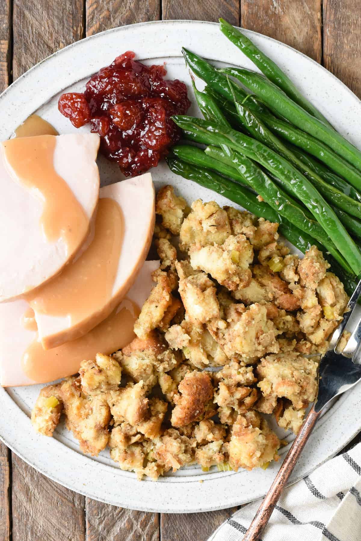Plate of Thanksgiving dinner, with turkey and gravy, bread stuffing, cranberry sauce and green beans.