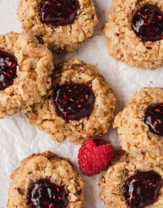 Raspberry thumbprint cookies on white parchment paper.