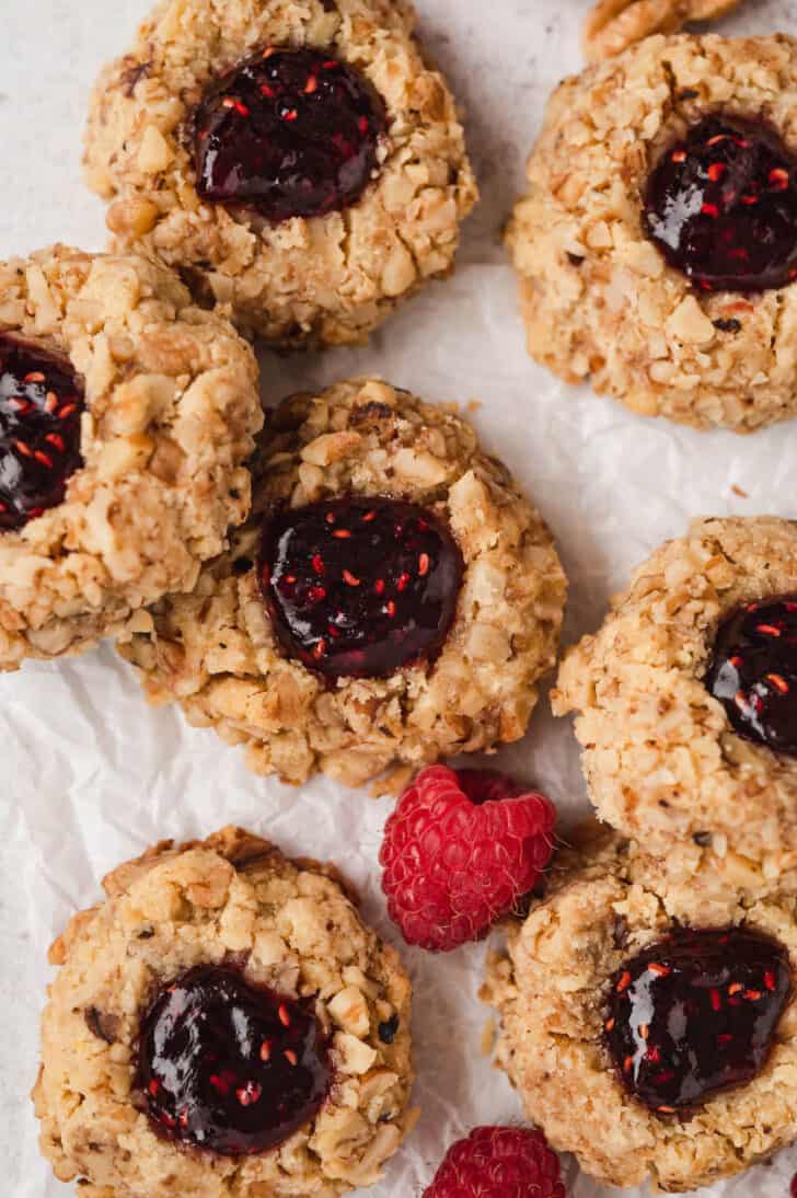 Raspberry thumbprint cookies on white parchment paper.