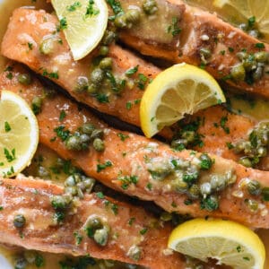 Salmon piccata in a white skillet, garnished with lemon wedges.