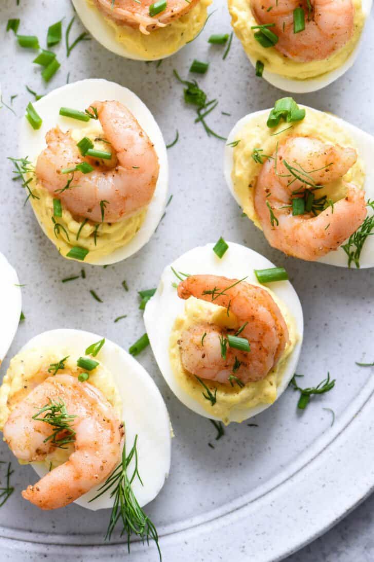 Dressed hard boiled eggs garnished with seafood and herbs on a light gray plate.