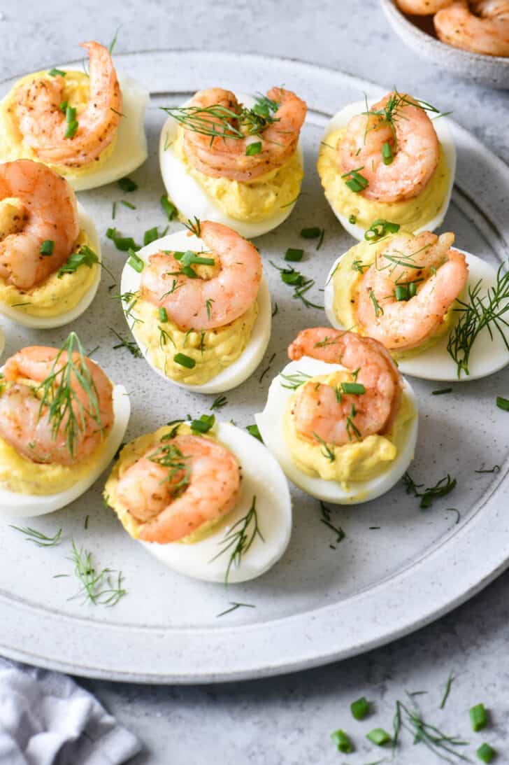 Easter appetizer made with eggs and seafood, garnished with chives and dill on a light gray plate.