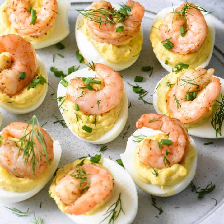Shrimp deviled eggs garnish with chives and dill on a light gray plate.