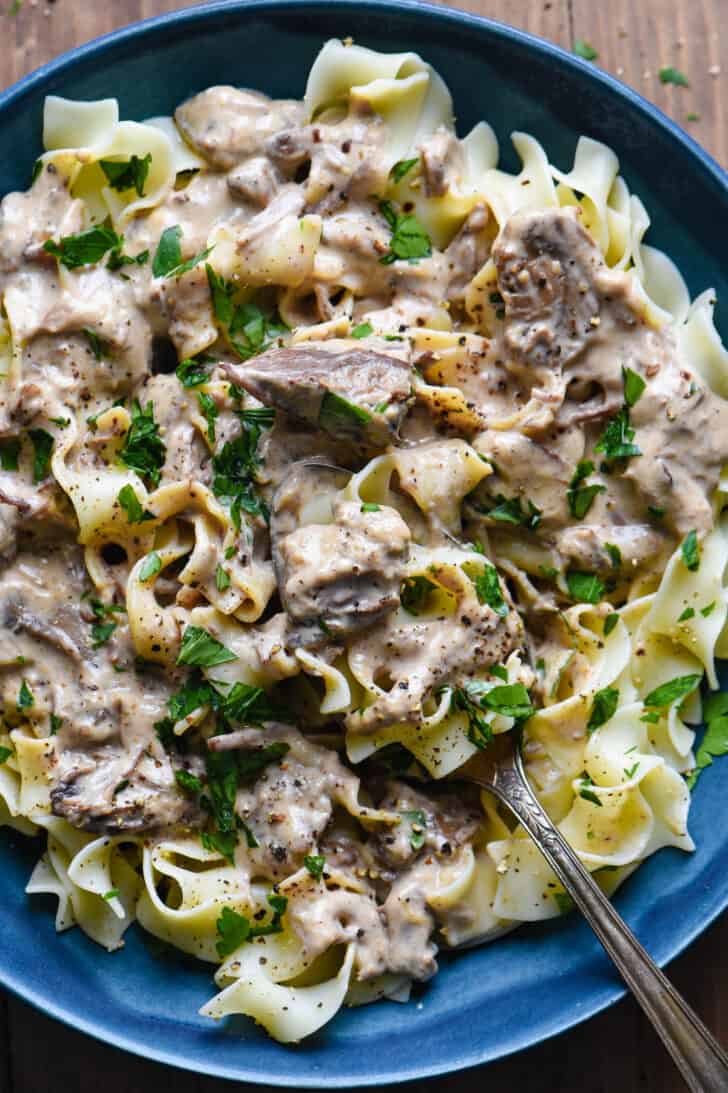 A blue bowl filled with creamy beef stew with egg noodles.