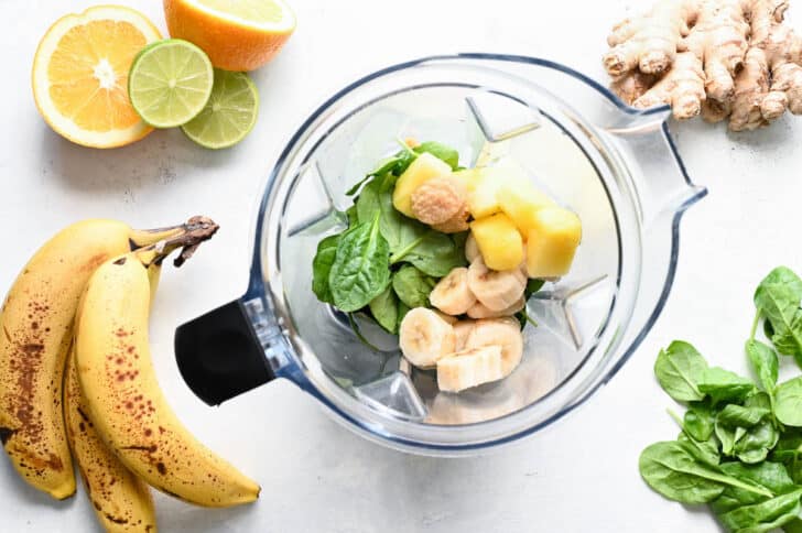 Bananas, pineapple, spinach and ginger in a blender pitcher.
