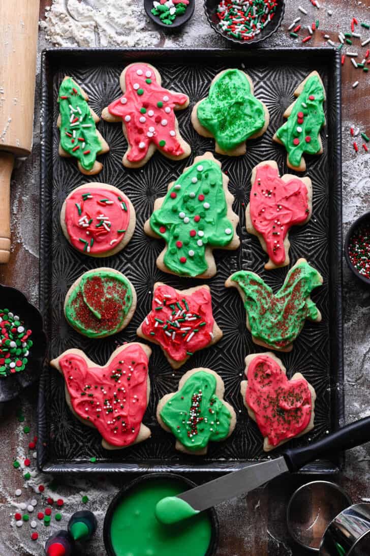 Frosted Sour Cream Cookies with sprinkles in a variety of shapes on a textured baking pan.