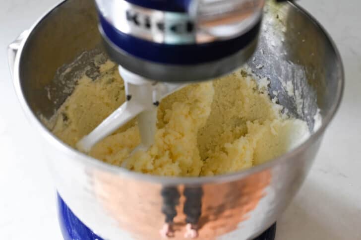 A mixture of flour and sugar in a Kitchenaid stand mixer bowl being beat with the paddle attachment.